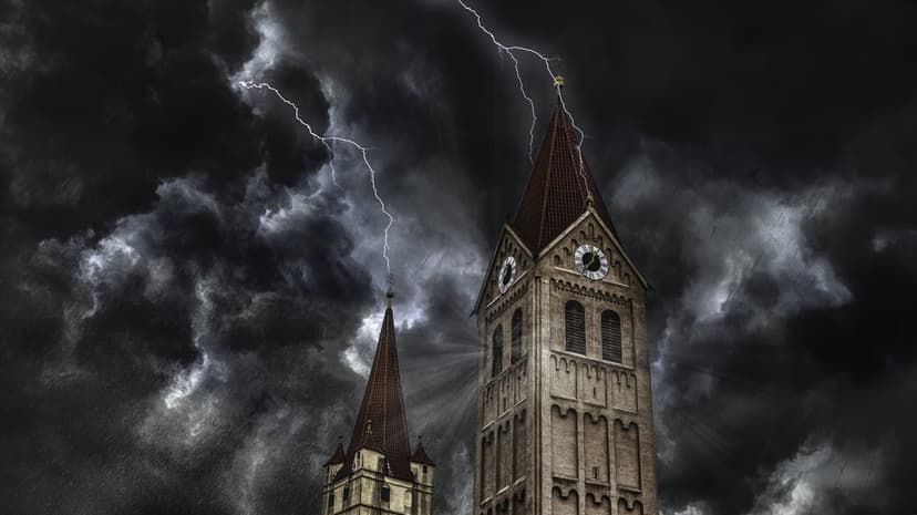 Two stone church spires with a clock face are illuminated by a bright lightning strike under a dark stormy sky.