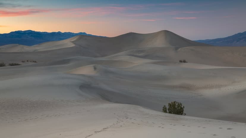 Towering sand dunes feature sharp ridges and ripple patterns under a soft pastel twilight sky in the desert.