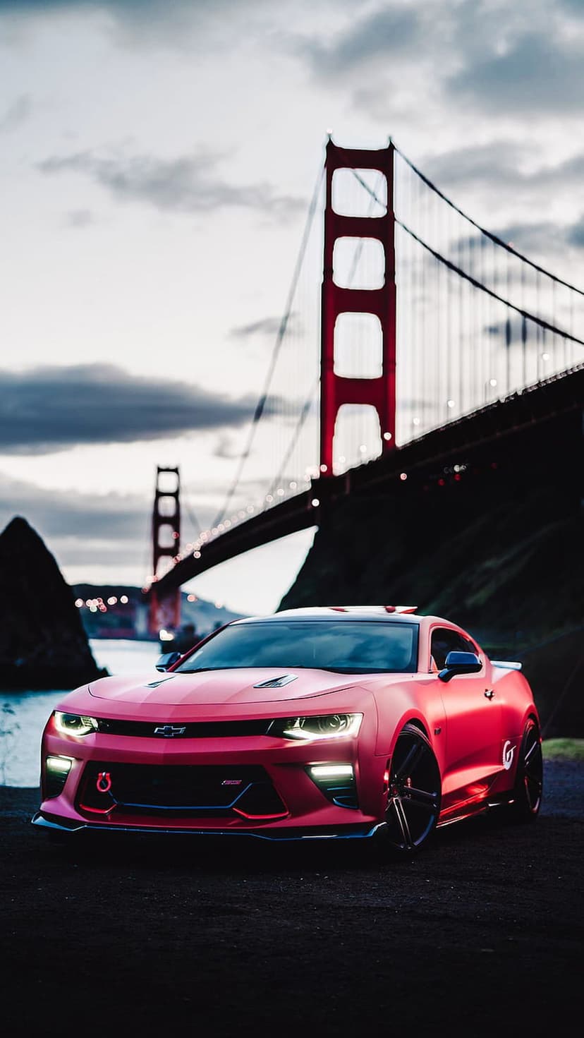 Red Chevrolet Camaro parked on a road with the Golden Gate Bridge towers and a purple dusk sky in the background.
