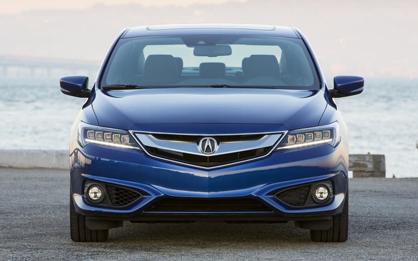 Front view of a blue Acura ILX with LED headlights on a pier with water and a distant bridge in the background.