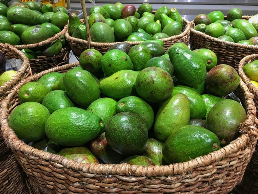 Fresh green avocados stacked inside rustic woven wicker baskets at an outdoor farmers market produce stall.