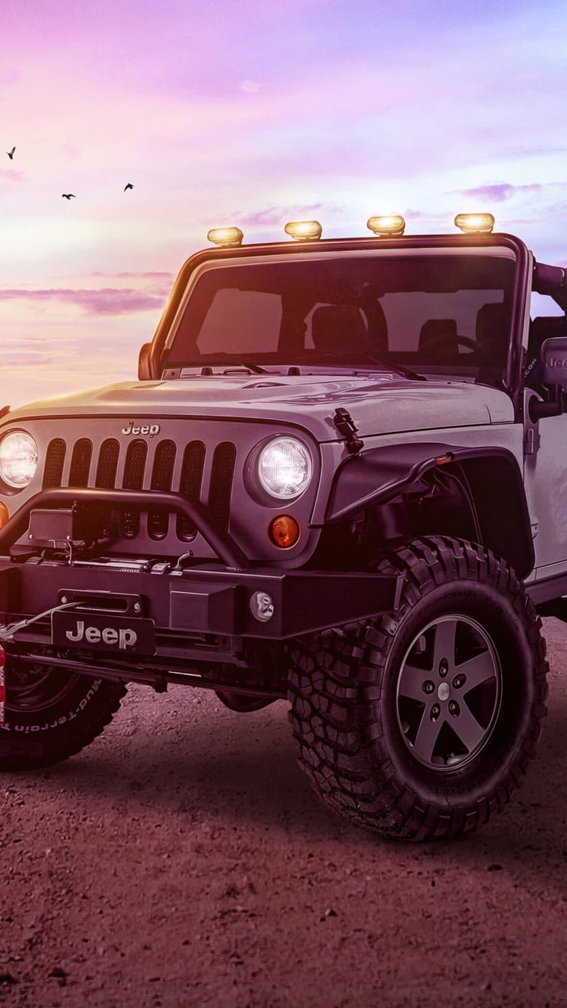 Silver off-road Jeep Wrangler with roof lights on a dirt road under a pink and purple sunset sky.