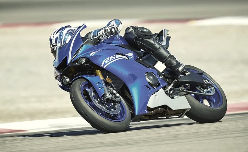 Blue Yamaha R6 sportbike leaning deep into a racetrack turn with a rider in black leathers and helmet.