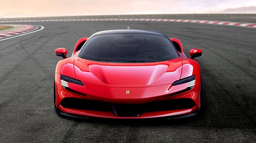 Front view of a red Ferrari supercar on an asphalt racetrack with red and white curbing under a soft sky.