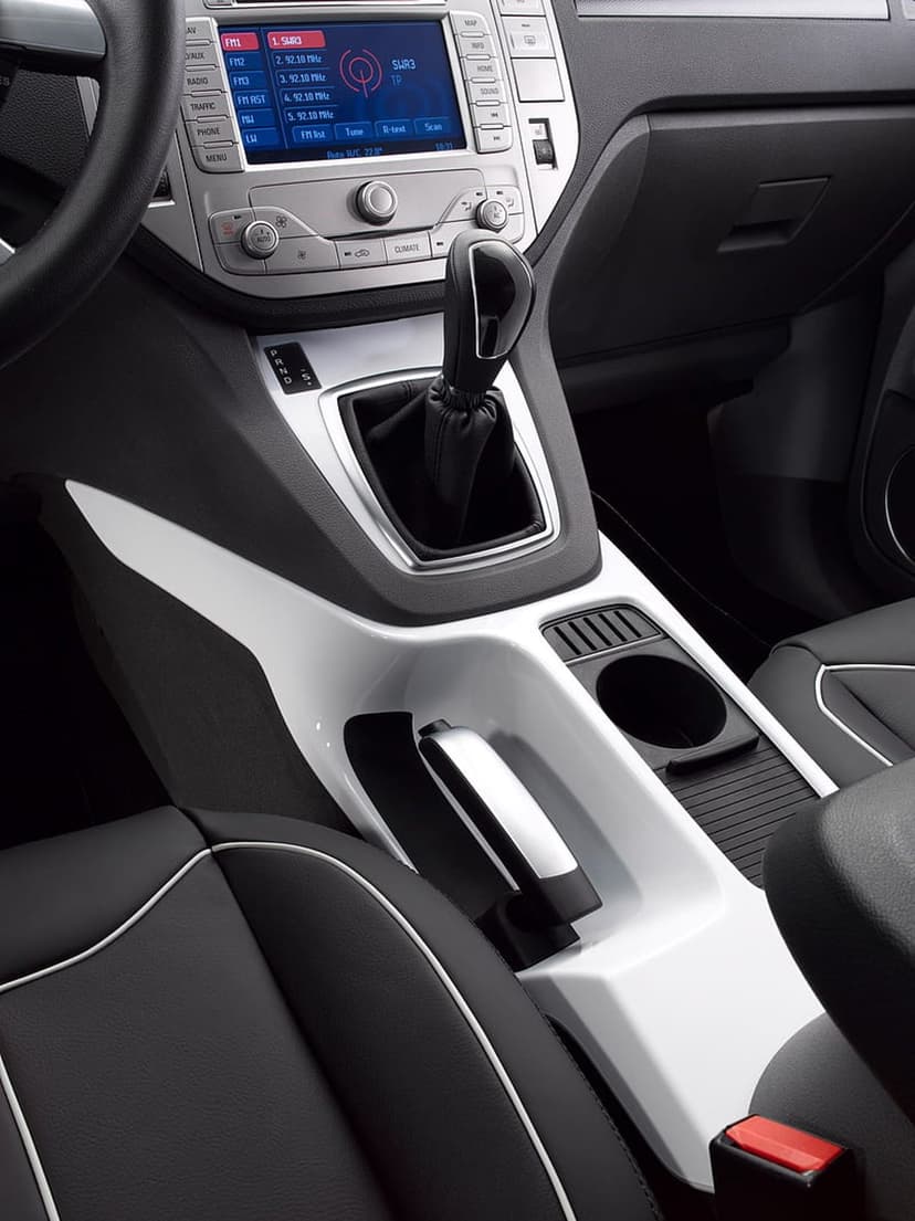 Modern car dashboard with a touchscreen display, gear shifter, and black leather seats with white stitching.