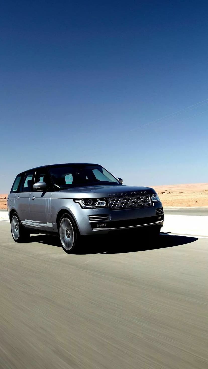 Silver luxury SUV driving on a desert highway under a clear blue sky with motion blur on the road surface.