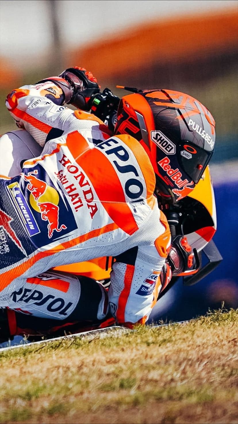 MotoGP racer in a Repsol Honda suit leans low on a motorcycle during a high-speed turn on a racing track.