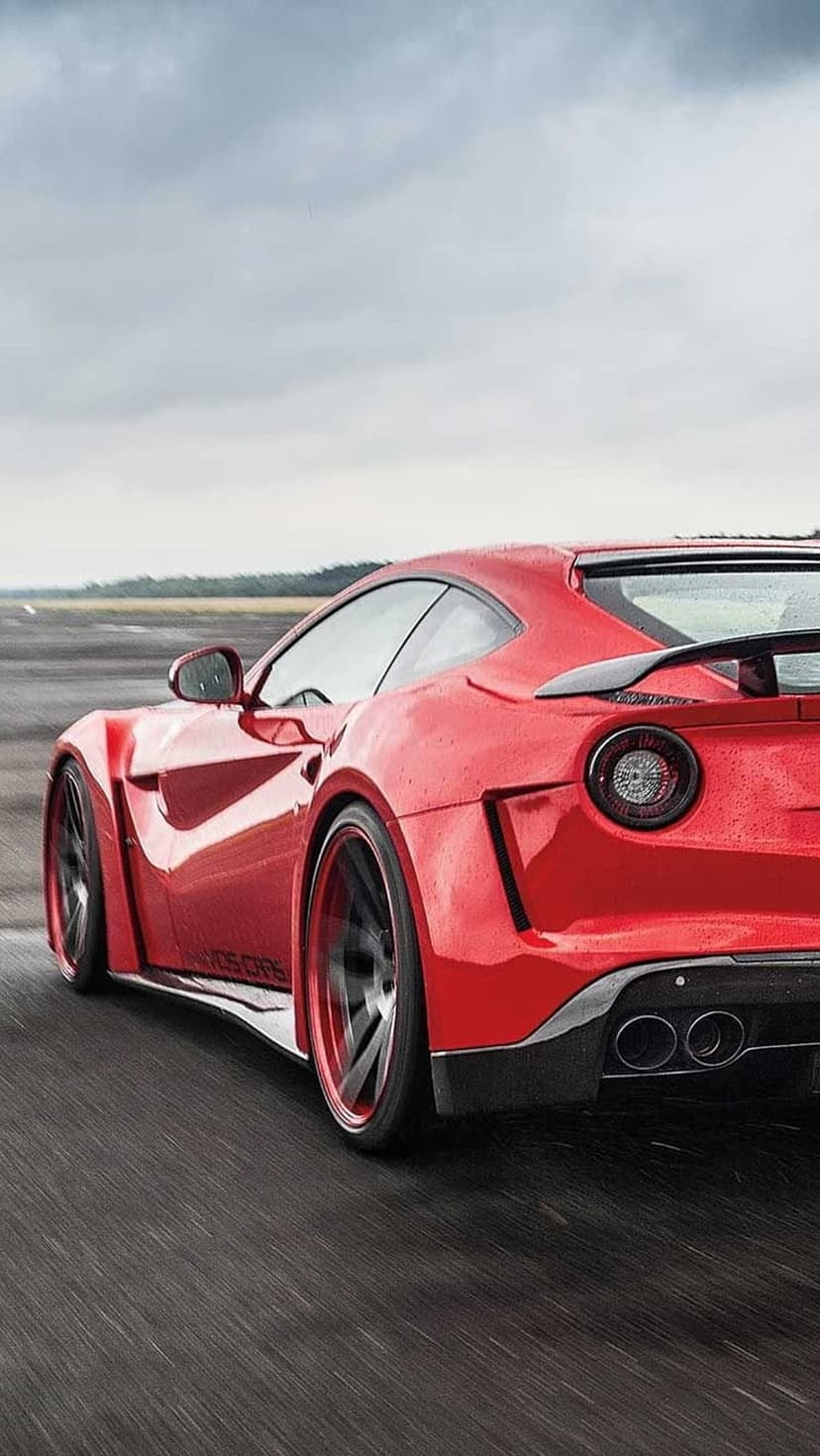 Red Ferrari F12tdf speeding on a wet racetrack with motion blur, wide body kit, and a cloudy sky backdrop.