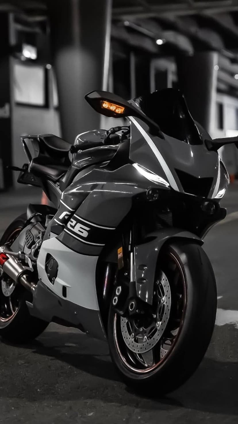 Yamaha R6 sportbike with dark grey fairings and white accents stands in a moody, low-lit studio environment.
