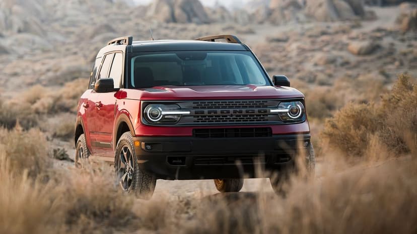 Red Ford Bronco Sport with glowing LED headlights parked on a rocky desert trail with dry grass.