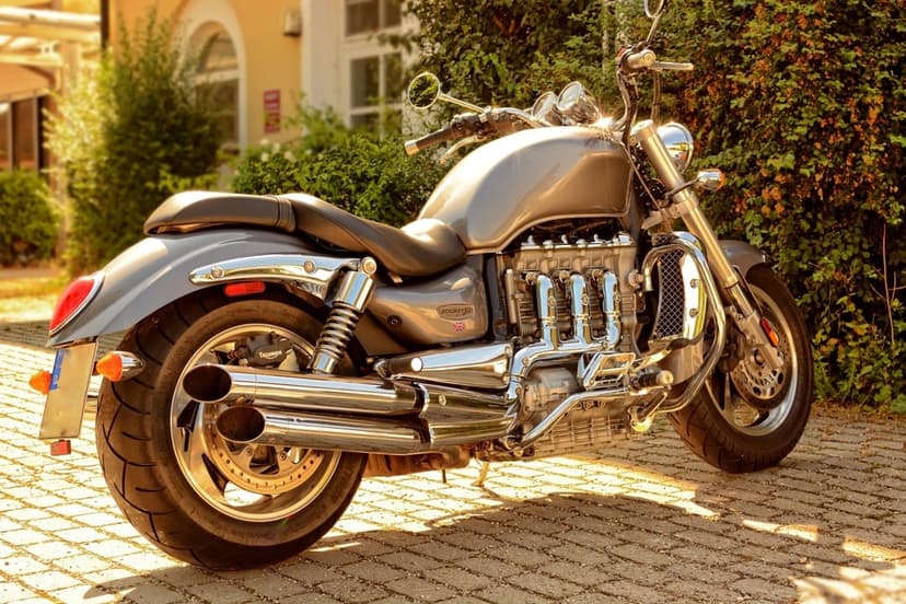 Silver Triumph Rocket III motorcycle with chrome pipes on a cobblestone path in warm golden hour sunlight.