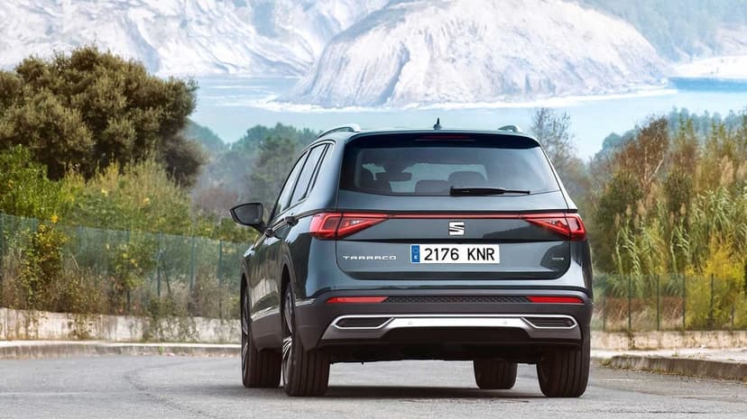 Rear view of a dark grey SEAT Tarraco SUV on a mountain road with misty coastal cliffs in the distance.