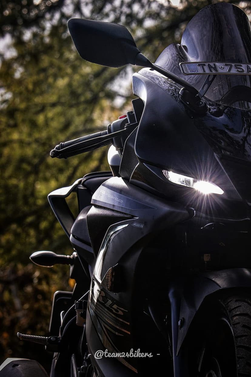 Yamaha R15 motorcycle with a glowing starburst headlight parked outdoors against a soft blurred forest background.