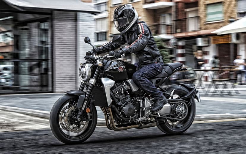 Black sport motorcycle with rider in leather gear moving through a blurred city street with outdoor cafes.