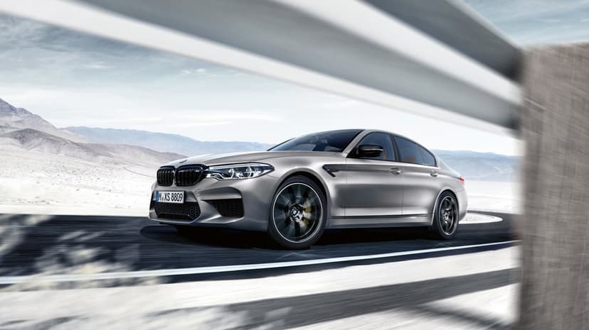 Silver BMW M5 luxury sedan driving on a winding mountain road with motion blur wheels and desert background.