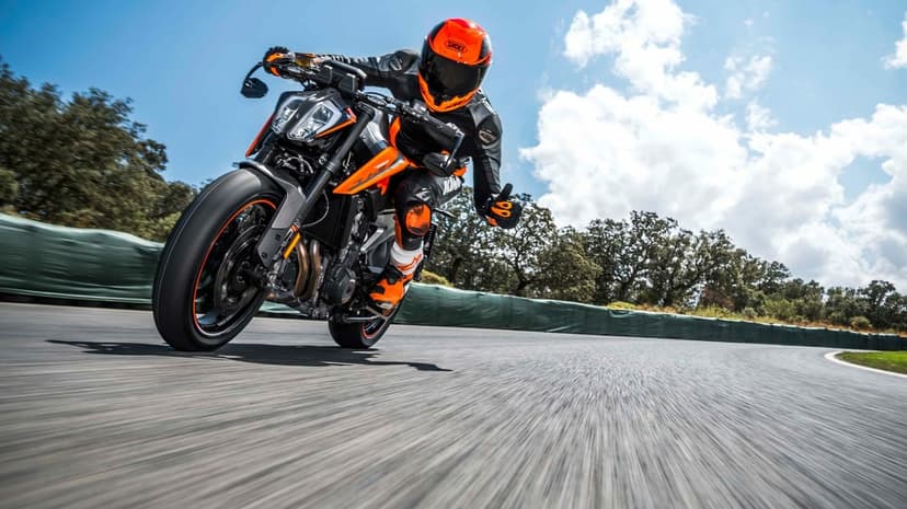 A motorcyclist in orange gear leans a KTM sportbike into a turn on a racetrack under a bright blue sky.