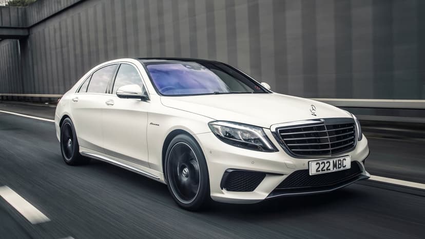 White Mercedes-Benz AMG sedan driving on a highway with motion-blurred wheels and a grey textured wall background.