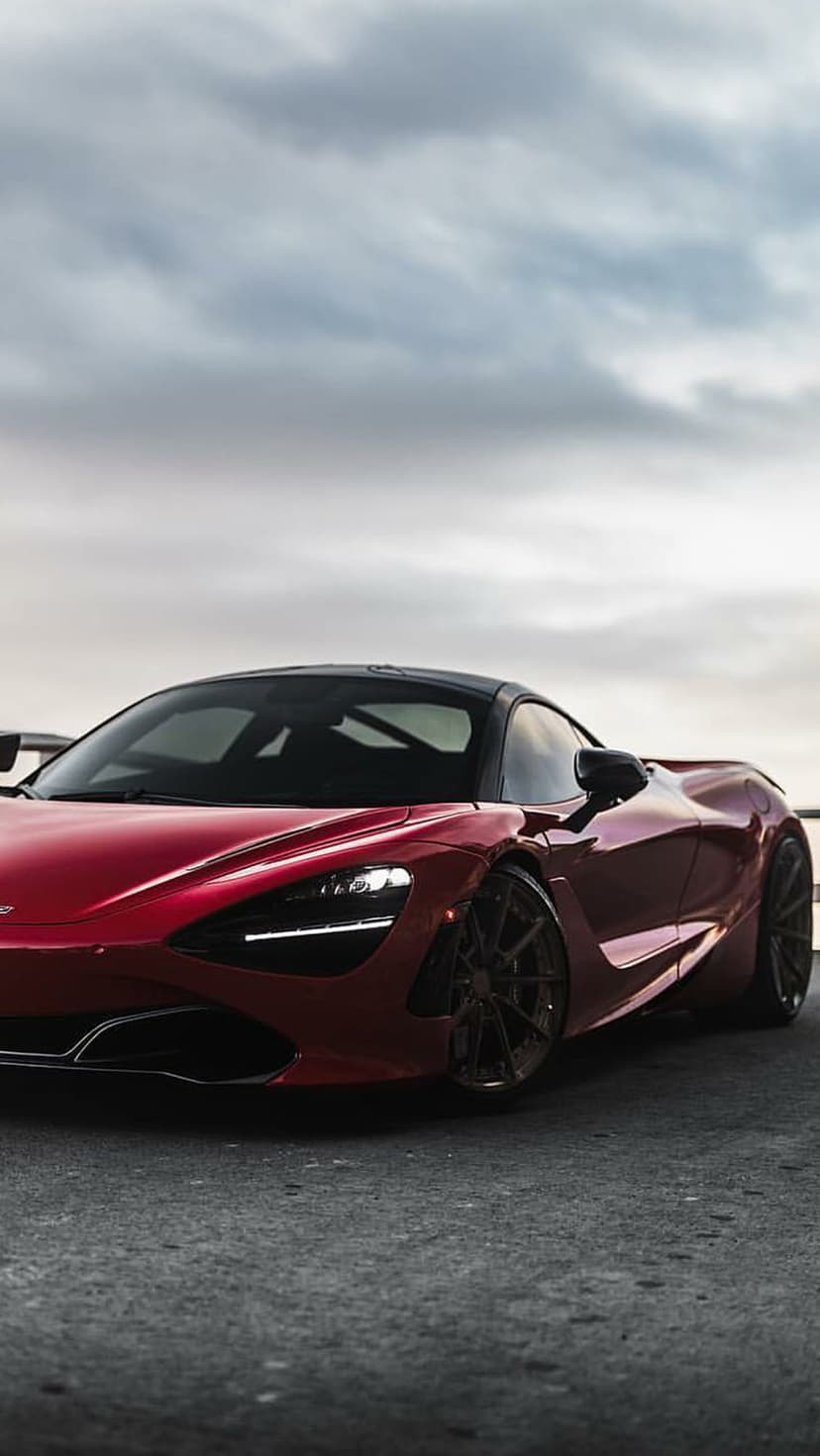 Red McLaren 720S supercar with a black roof parked on dark asphalt under a dramatic and cloudy grey sky.