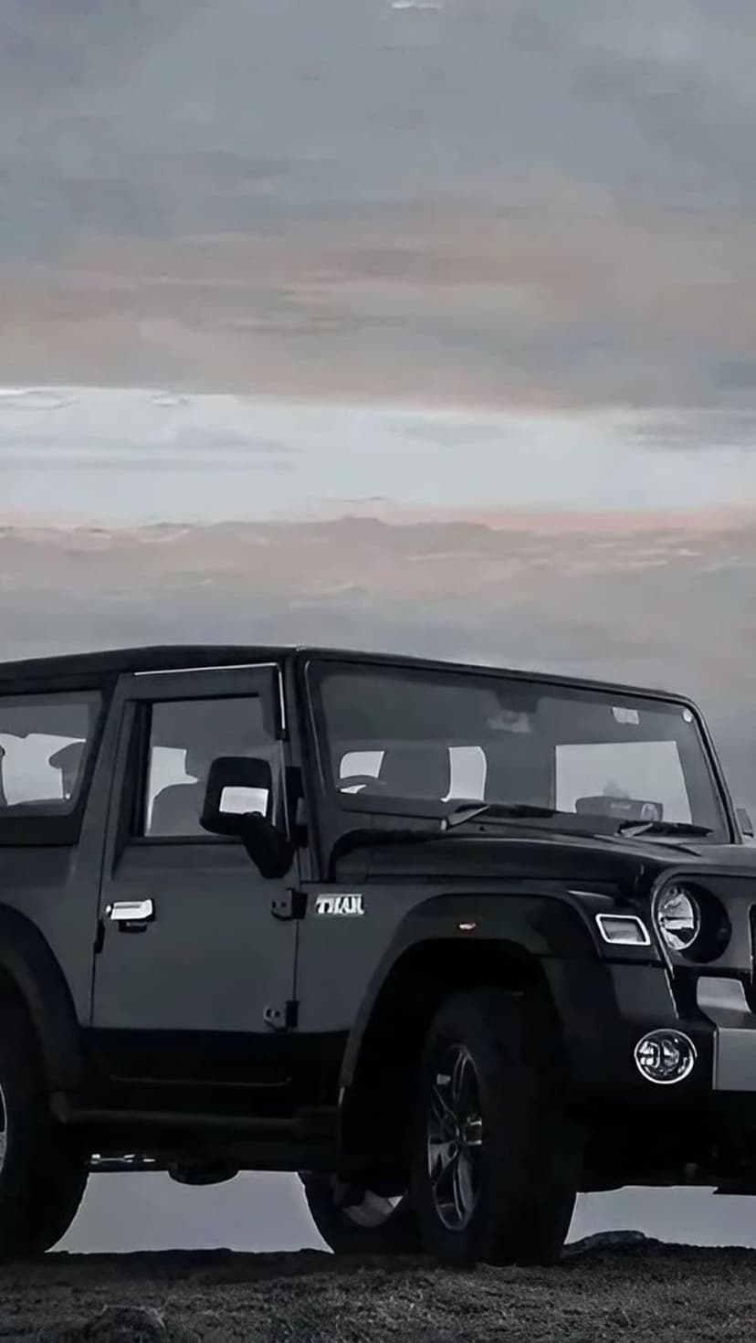Black Mahindra Thar SUV parked under a heavy, dramatic sky with soft light reflecting off its dark metallic body.