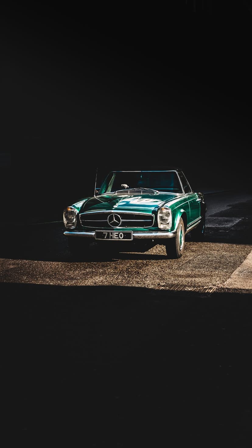 Vintage emerald green Mercedes convertible with a 7 HEO license plate parked on asphalt in dark moody lighting.