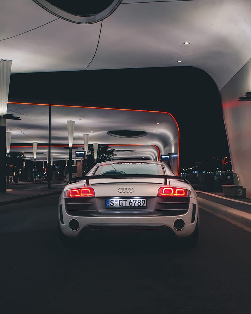 White Audi R8 rear view parked at a glowing orange gas station at night with sleek architectural lighting.