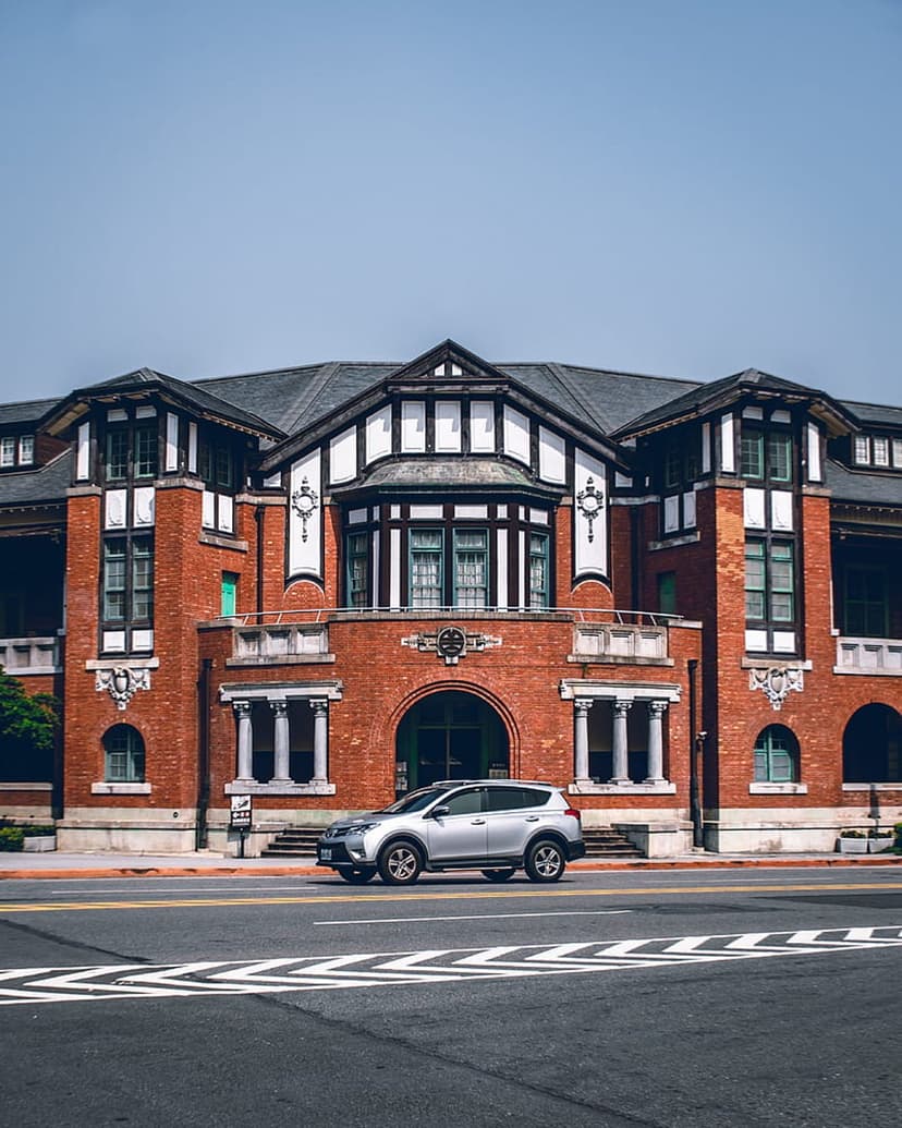Red brick building with white window trim overlooks a silver SUV parked on a street with a white crosswalk.