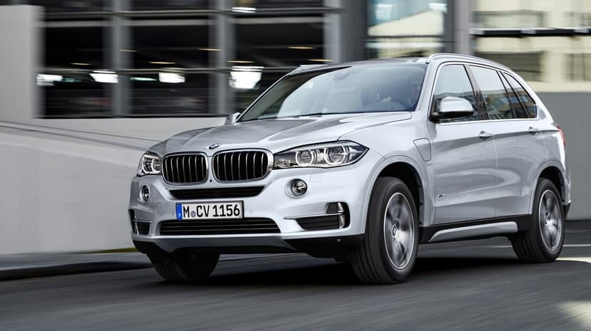 Silver BMW X5 SUV driving on a city street with motion blur wheels and sleek metallic reflections.