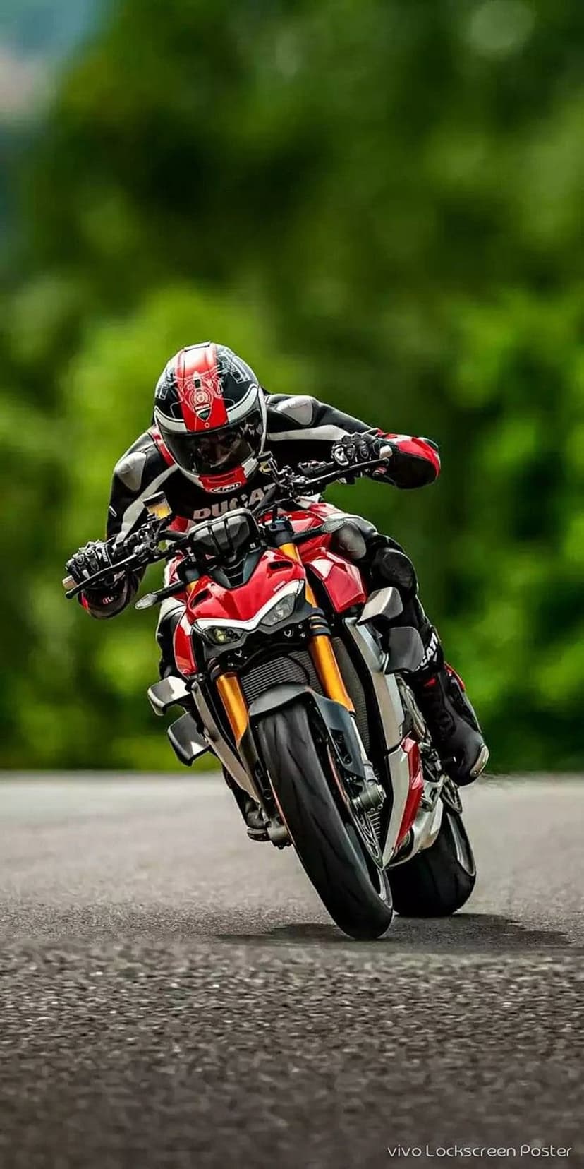Red motorcycle racer leaning deep into a road curve against a blurred background of green forest trees.