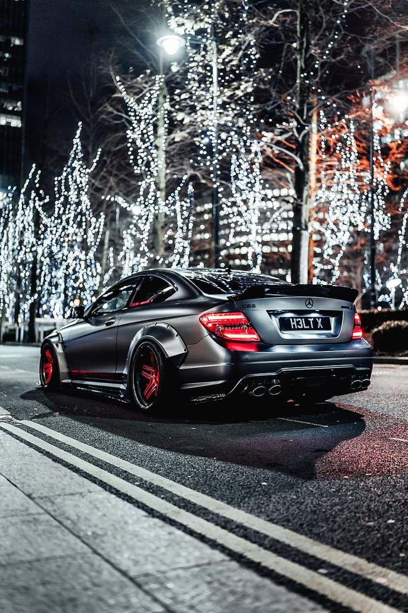Mercedes C63 AMG with widebody fenders and red wheels parked on a city street under festive Christmas lights.