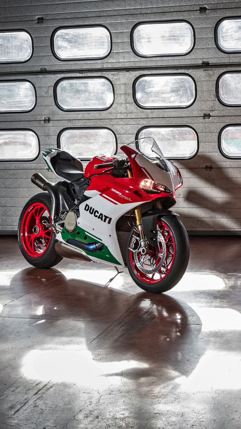 Ducati sportbike with red, white, and green fairings reflects on a polished concrete floor in a modern garage.