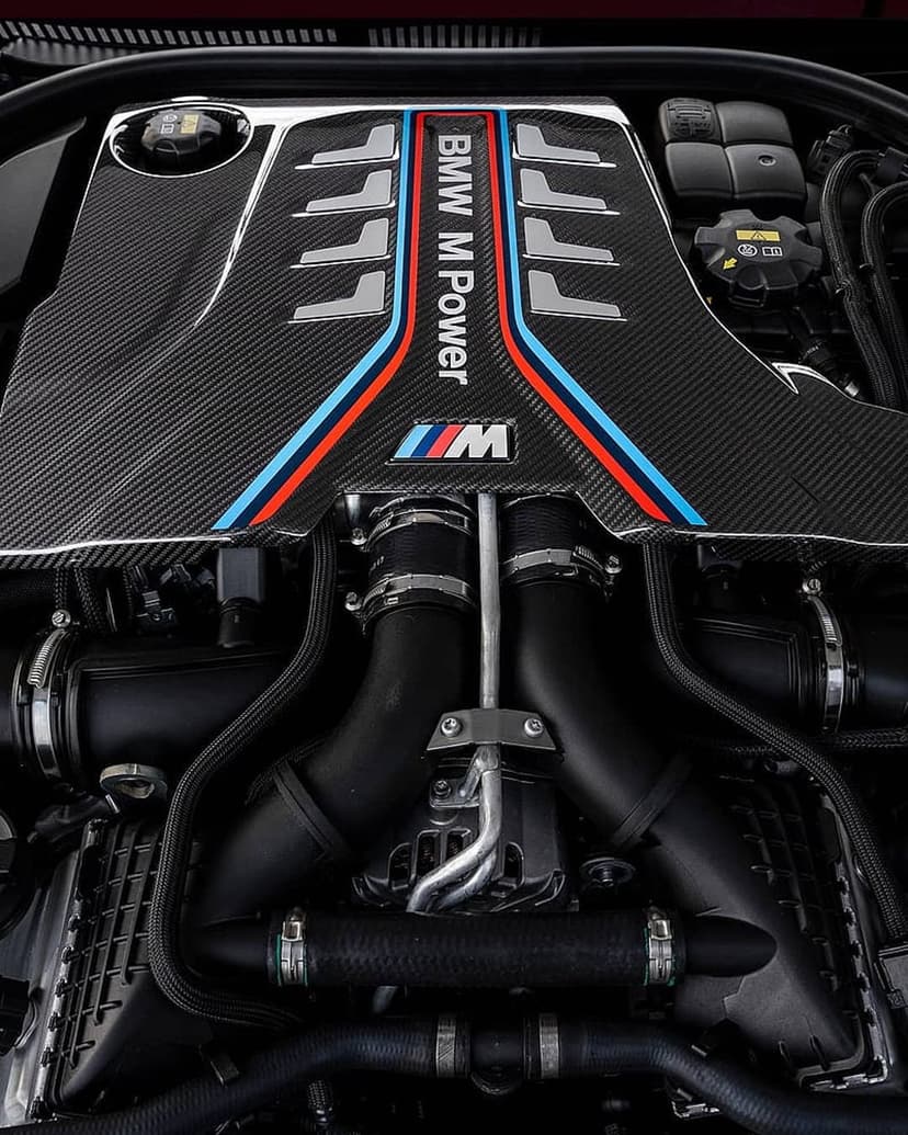 BMW M Power engine featuring a carbon fiber cover with signature colored stripes and detailed intake pipes.