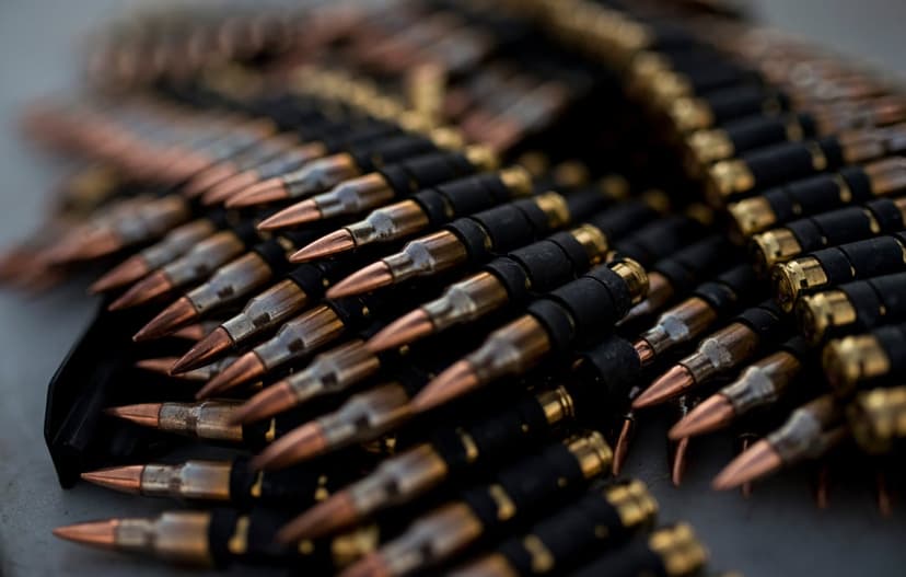 Linked brass machine gun cartridges with copper tips and metallic links shown in a sharp, vertical close-up view.