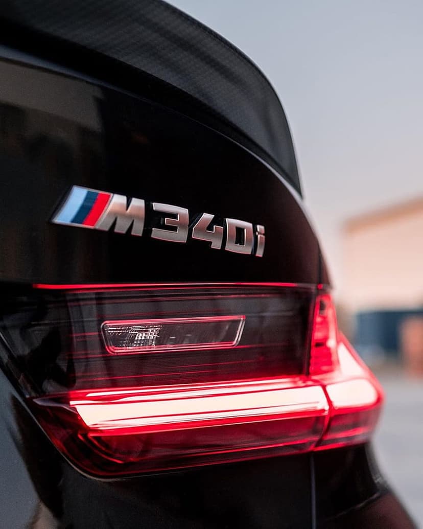 BMW M340i rear tail light with an illuminated red LED strip and a tricolor M badge on black metallic car paint.