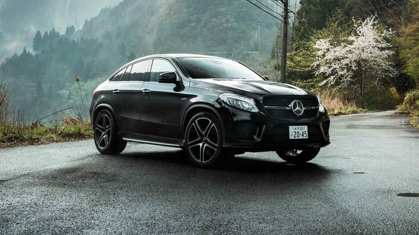 Black Mercedes-Benz GLE Coupe parked on a wet mountain road with misty green hills and cherry blossoms in Japan.