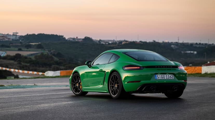 Green Porsche 718 Cayman GTS 4.0 on a racetrack during sunset with rolling hills and a soft twilight sky.