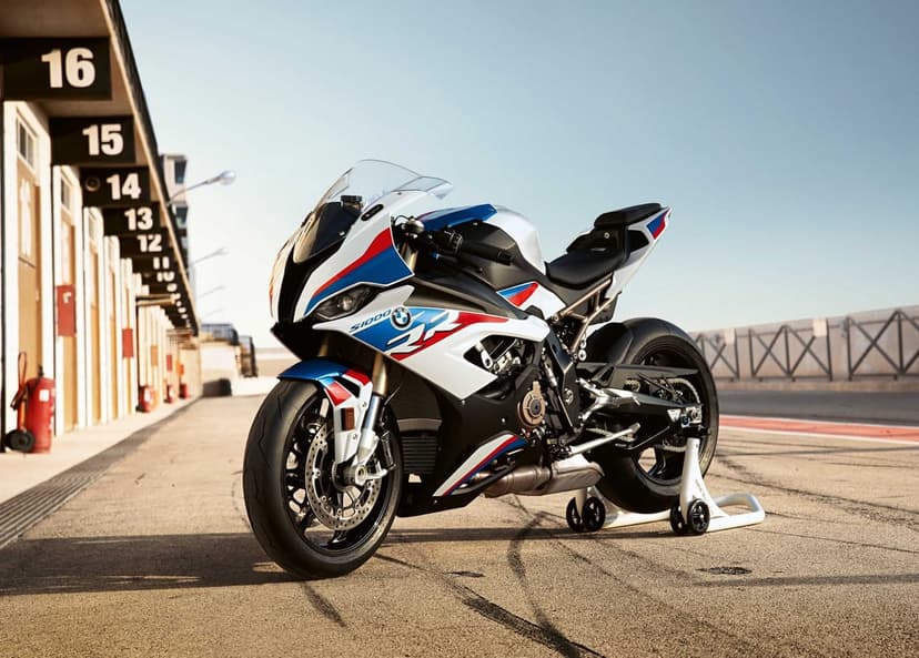BMW S1000RR motorcycle in white, blue, and red colors parked on a racetrack pit lane under a clear sky.