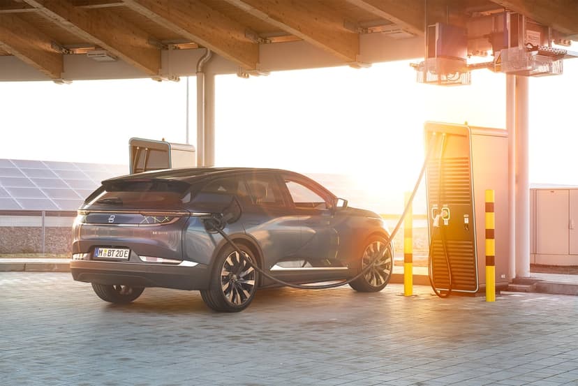 Blue electric SUV charging at a station during sunset with solar panels and golden lens flare background.