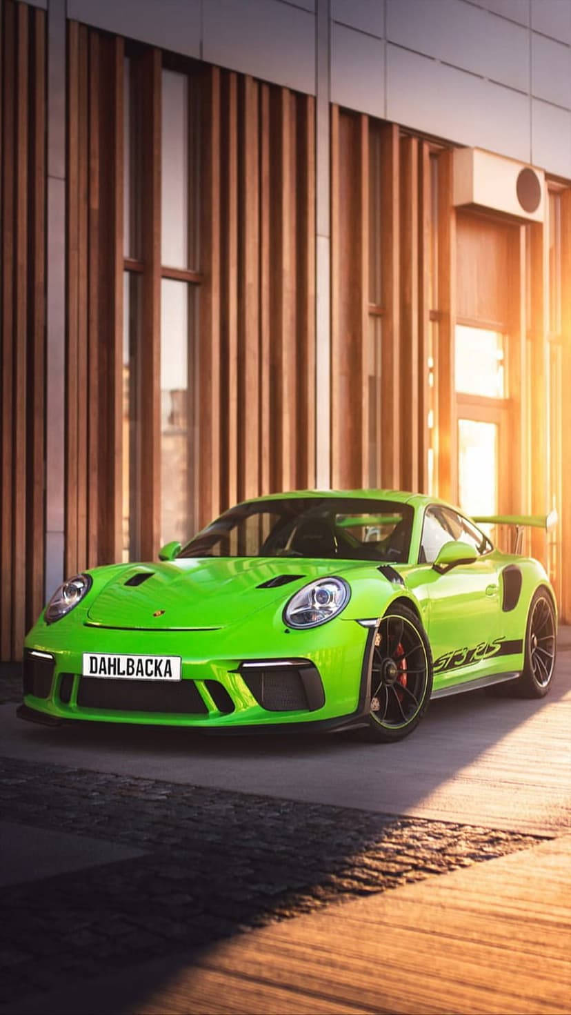 Porsche GT3 RS in lime green parked beside a wooden slatted building with aggressive aerodynamic styling.