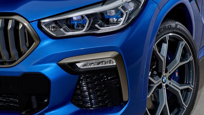Close-up of a blue BMW front headlight, metallic grille, and performance wheel with blue M brake calipers.