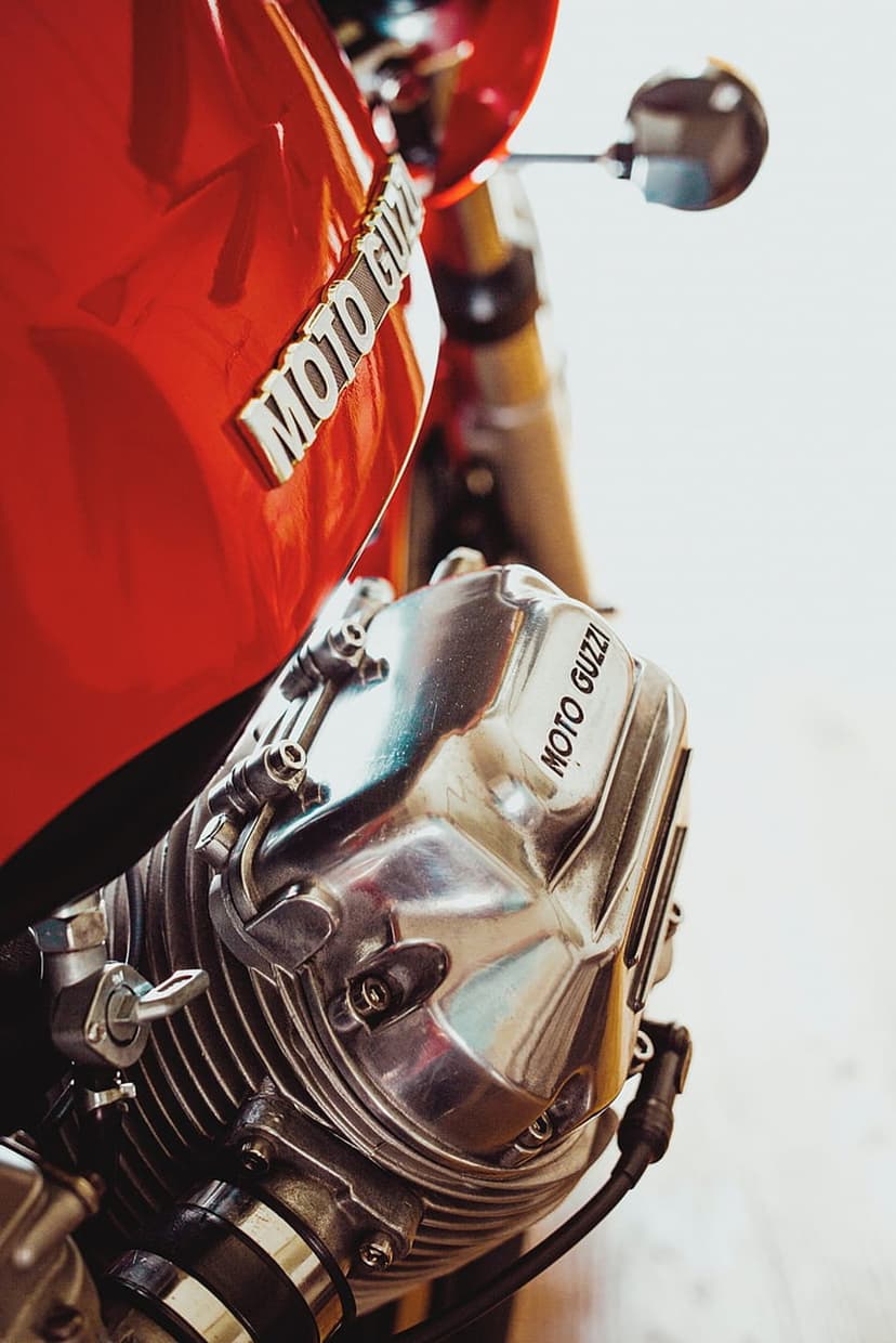 Red Moto Guzzi fuel tank and chrome engine cylinder with cooling fins showing the brand logo in sharp detail.