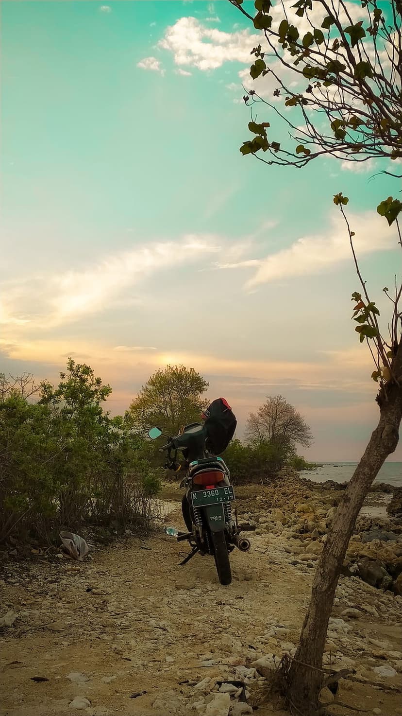 Black motorcycle on a rocky coast overlooking the ocean under a pastel orange and teal twilight sky.
