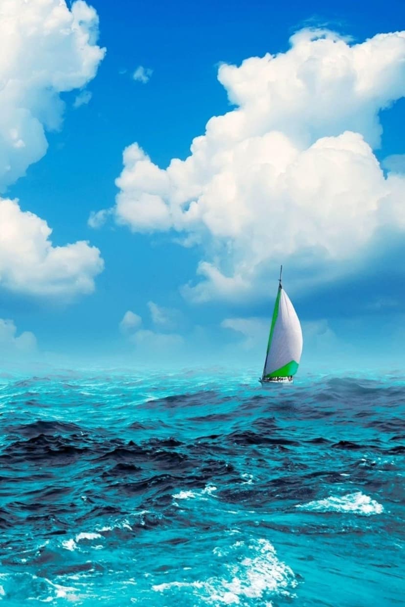 Sailboat with white and green sails navigating bright turquoise ocean waves beneath a blue sky with white clouds.