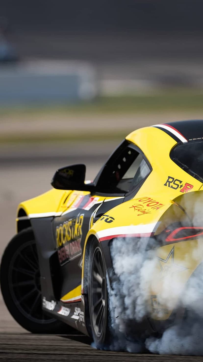 Yellow Toyota Supra drifting with white tire smoke, featuring Rockstar decals on a vertical mobile background.