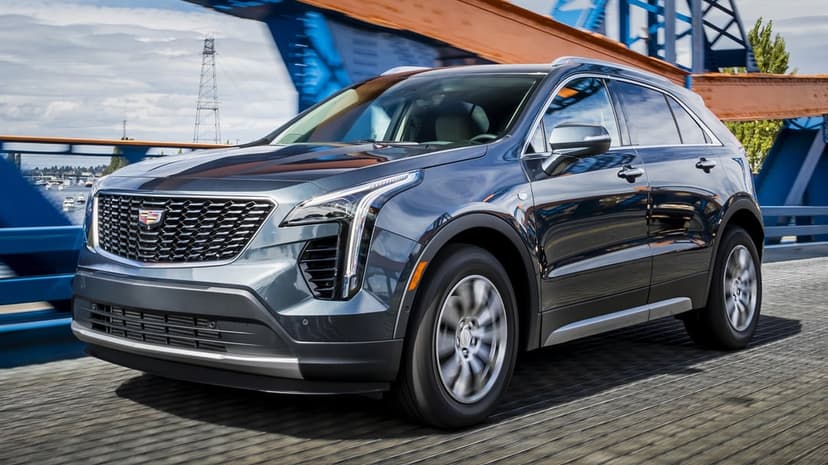 Dark grey luxury SUV driving on a blue and orange bridge with motion-blurred wheels and scenic city backdrop.