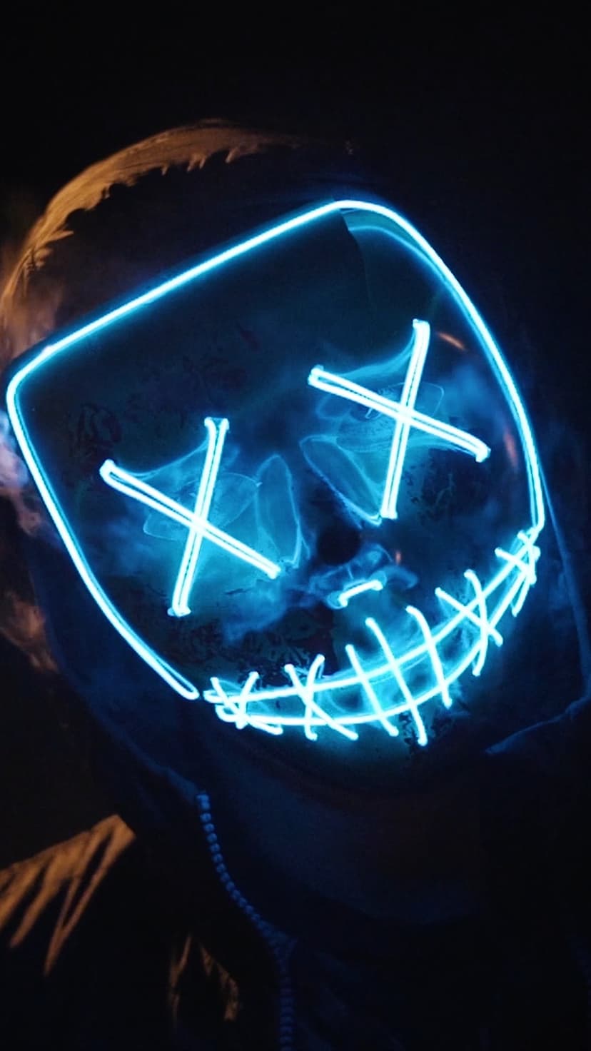 Person wearing a black mask with blue neon X-shaped eyes and a glowing smile surrounded by thin white vapor.
