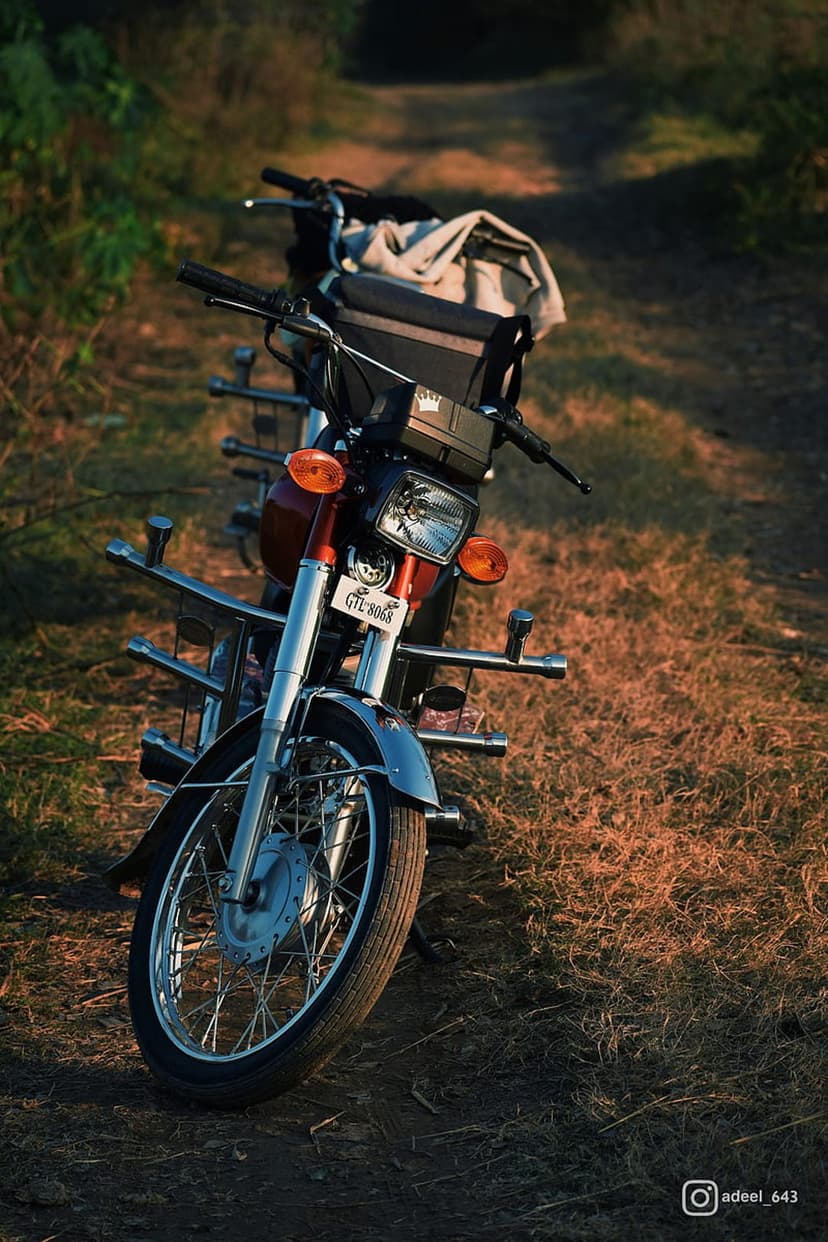 Red vintage motorcycle with chrome details parked on a grassy dirt trail during a warm golden hour sunset.