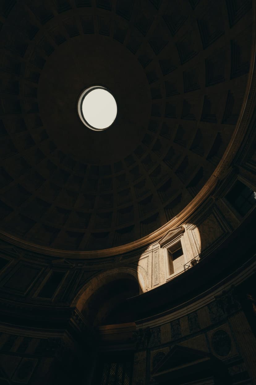Pantheon dome oculus with a bright sunbeam illuminating geometric stone coffers and deep shadows in Rome, Italy.