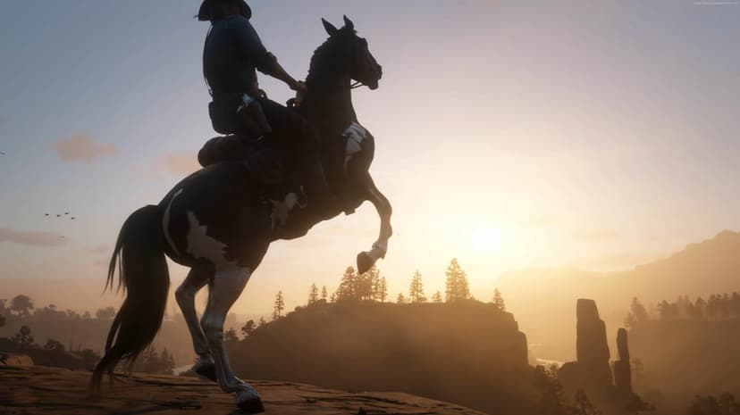Cowboy on a rearing horse silhouetted against a golden sunset on a rocky cliff overlooking a hazy valley.
