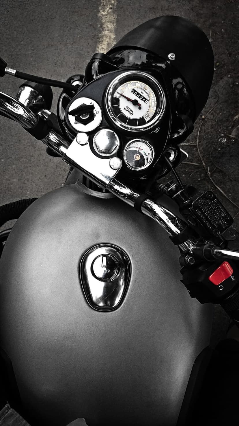 Royal Enfield handlebars and chrome fuel tank with an analog speedometer shown in a detailed monochrome close-up.