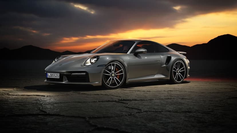 Silver sports car parked on a cracked desert floor during a dramatic golden hour sunset with mountain peaks.